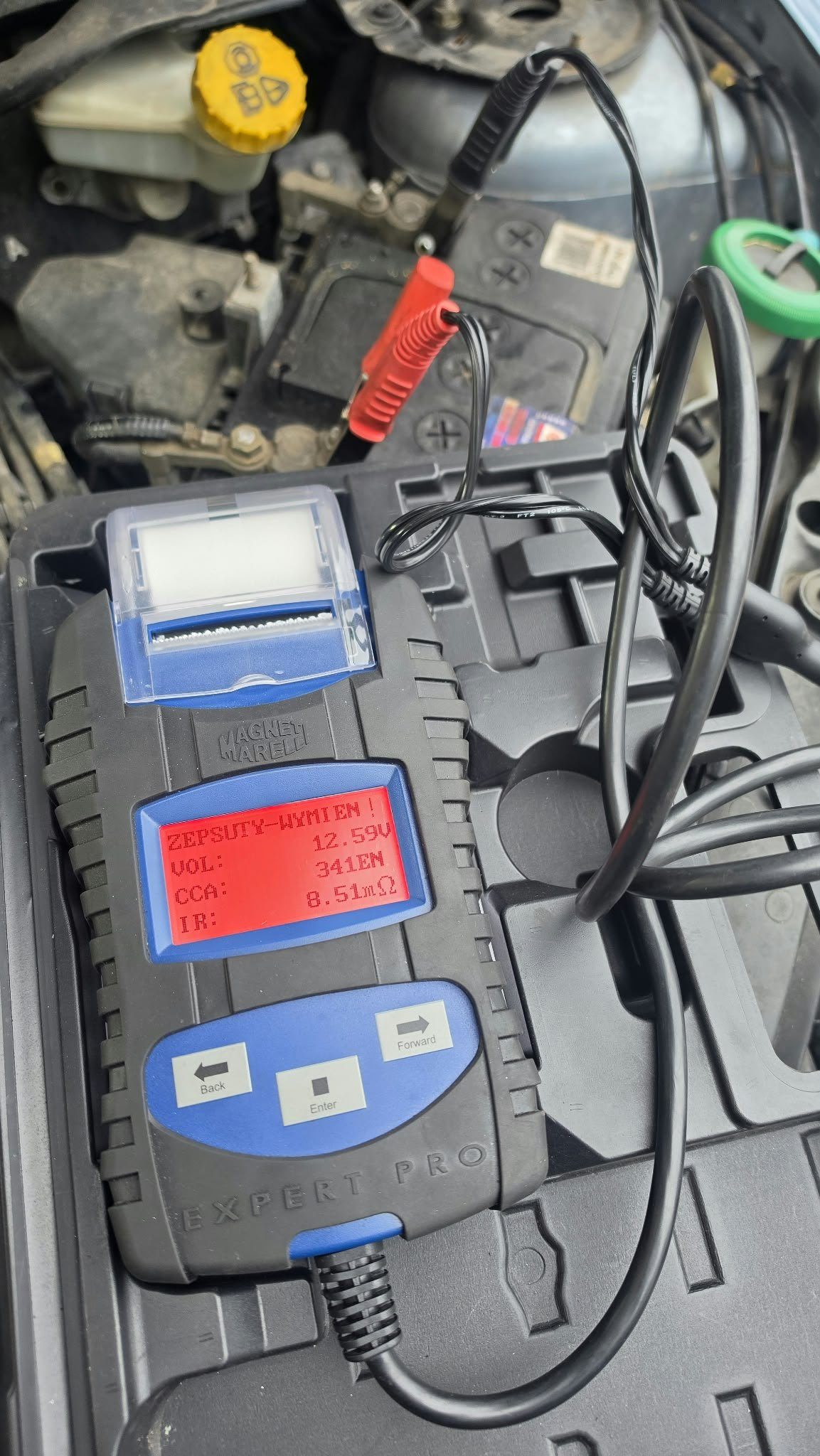 Tester akumulatorów Magneti Marelli Expert Pro podłączony klemami do akumulatora w komorze silnika, na ekranie wynik testu